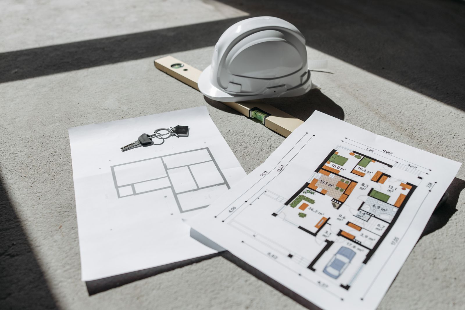 A white hard hat and a spirit level resting on colour floor-plan sheets in bright sunlight