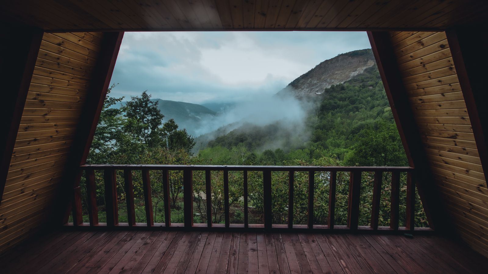 A covered timber balcony framing a view out to misty forested mountains